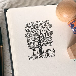 Puede incluir: Un sello en blanco y negro con un dise&ntilde;o de &aacute;rbol y el texto "Ex Libris Anna Gulligan".