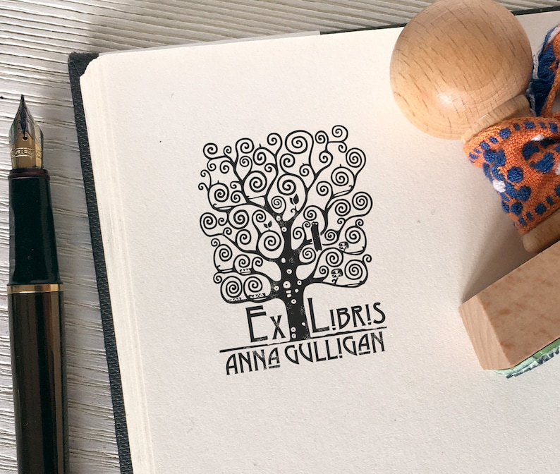 Puede incluir: Un sello en blanco y negro con un dise&ntilde;o de &aacute;rbol y el texto "Ex Libris Anna Gulligan".