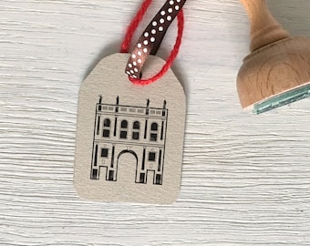 May include: A brown paper gift tag with a black and white illustration of a building with an archway. The tag is tied with a red and white polka dot ribbon.