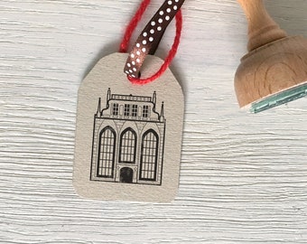 May include: A brown paper gift tag with a black and white illustration of a building with a pointed roof and windows. The tag is tied with a red and white polka dot ribbon.