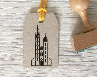 May include: A brown paper tag with a yellow string tied around it. The tag has a black and white illustration of a church with two towers.