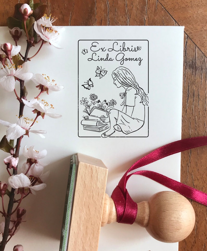 Girlish Bookplate Stamp. Unique stamp's illustration shows the longhaired girl sitting above the books and reading one. There are flowers and butterflies around. A premium quality stamp with the knob on top of the wooden handle.