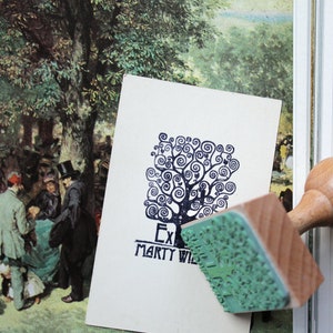 Puede incluir: Un sello de madera con una almohadilla de tinta verde. El sello presenta un dise&ntilde;o de &aacute;rbol estilizado con el texto "Ex Marty Wil" debajo.