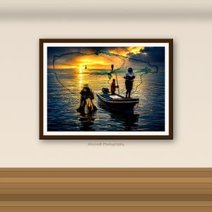 May include: A framed wall art print titled ShanniB Photography depicting a sunset scene over the ocean. A small boat with two figures is visible, one casting a large circular fishing net into the water against a bright golden horizon.