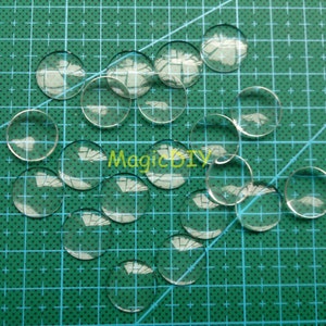 May include: A collection of clear round glass cabochons, scattered on a green cutting mat. The cabochons are various sizes and are perfect for crafting projects.