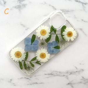 May include: A clear phone case with pressed flowers. The case features white daisies and blue hydrangeas.