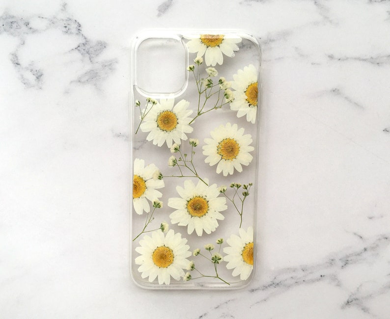 May include: A clear phone case with a pressed flower design. The case features white daisies with yellow centers and green stems.