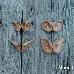 May include: Four pairs of brown, flexible, molded plastic ears, arranged in a pattern on a gray wooden surface. The ears are for crafting and costume making.