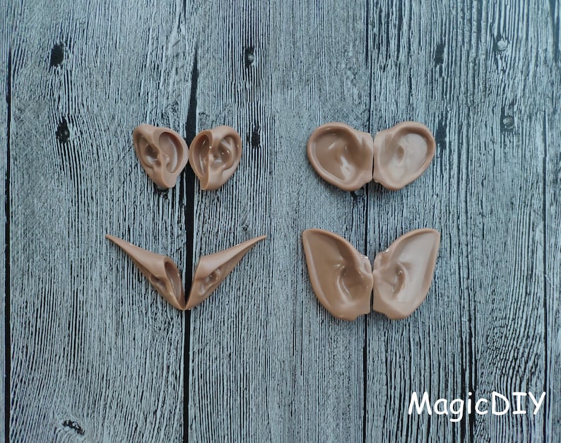 May include: Four pairs of brown, flexible, molded plastic ears, arranged in a pattern on a gray wooden surface. The ears are for crafting and costume making.