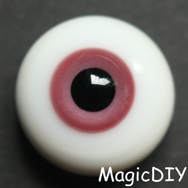 Pode incluir: Close-up de um olho de vidro realista com uma &iacute;ris rosa e uma pupila preta. O olho est&aacute; colocado sobre um fundo escuro.