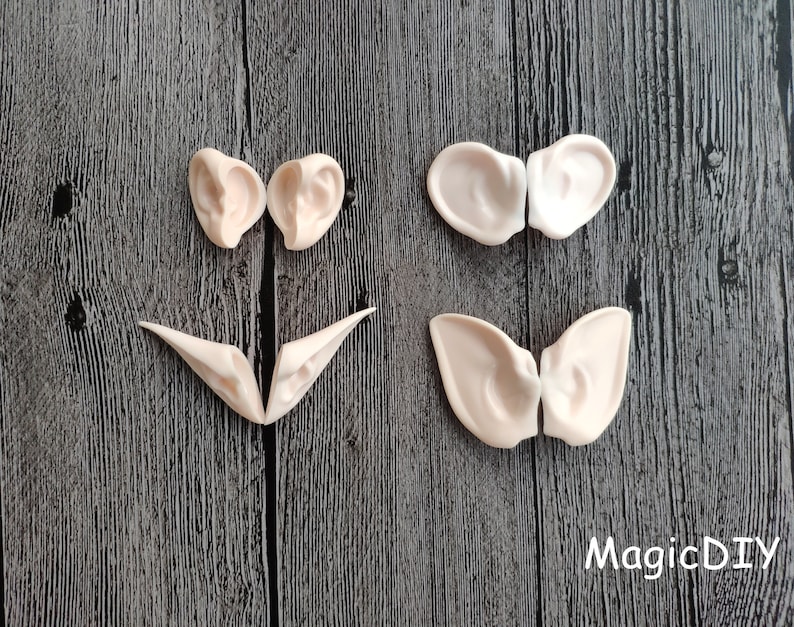 May include: Four pairs of elf ears made of a light beige colored material. The ears are in various shapes and sizes. The ears are on a dark wood background.