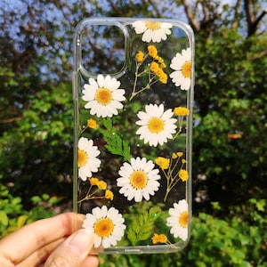 May include: A clear phone case with pressed white daisies and yellow flowers inside. The case is designed to fit a smartphone.