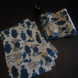 May include: Set of three blue and beige placemats with a sea life design. The placemats feature silhouettes of fish, crabs, and seahorses.