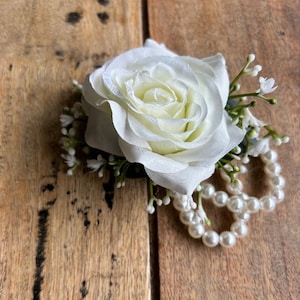 May include: A white silk rose with a pearl necklace, a wedding or prom corsage.