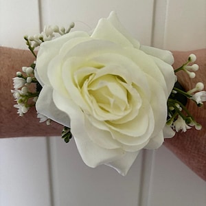 May include: A white rose boutonniere with small white flowers and green leaves.