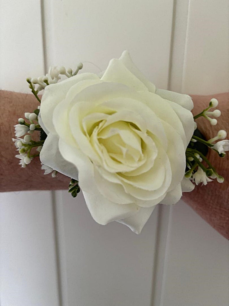 May include: A white rose boutonniere with small white flowers and green leaves.