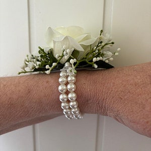 May include: A white rose with green leaves and white pearl beads on a wrist.