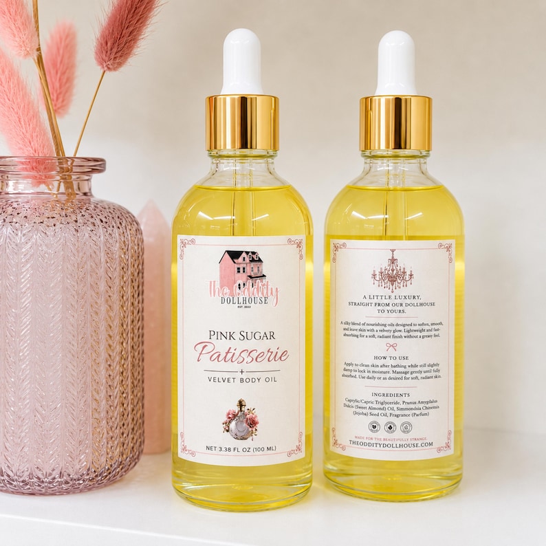 May include: Two clear glass dropper bottles filled with yellow body oil. The front label reads The Oddity Dollhouse Pink Sugar Patisserie Velvet Body Oil, net 3.38 fl oz. The back label includes instructions and ingredients for this skincare product.