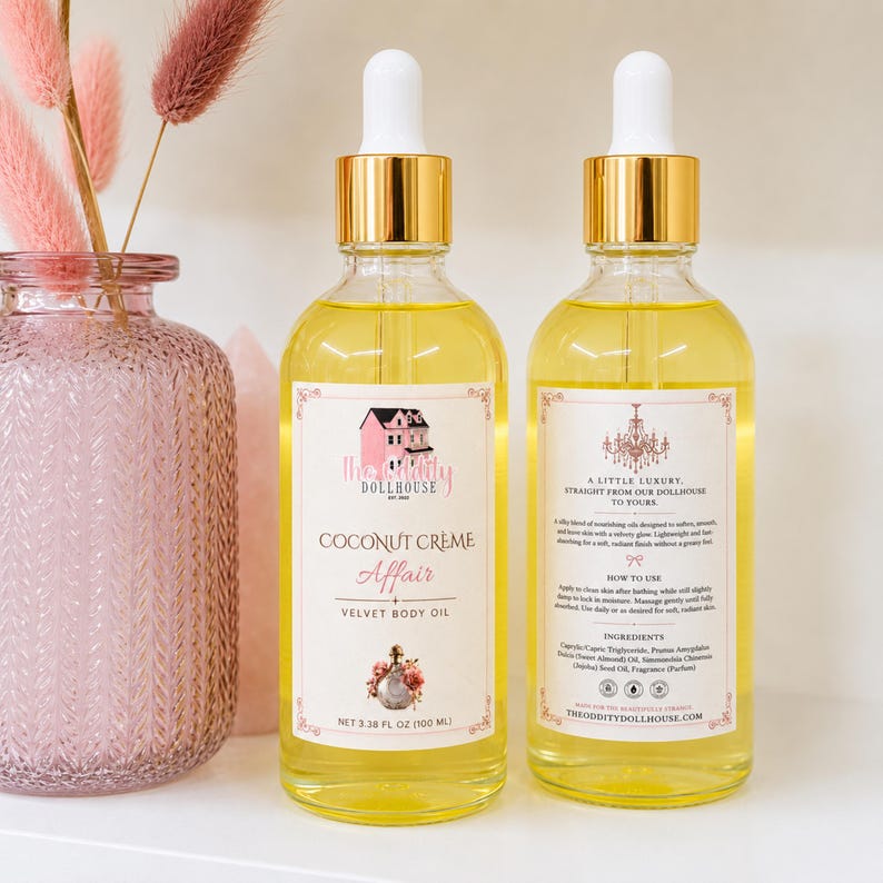 May include: Two clear glass bottles of Coconut Cr&egrave;me Affair velvet body oil with gold dropper caps. Each bottle contains 3.38 fl oz of yellow oil. The front label features a pink house illustration, while the back label lists ingredients.