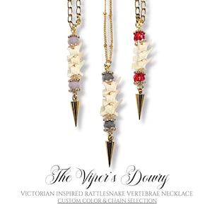 May include: Three gold-toned necklaces with a Victorian-inspired design. Each necklace features a chain, vertebrae, and a gold-colored cone pendant. The vertebrae are cream-colored, and the necklaces have red, gray, and purple accents. The text reads "The Viper's Dowry".