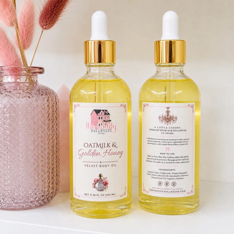 May include: Two clear glass dropper bottles filled with yellow body oil, featuring gold caps and white labels. The front label reads Oatmilk & Golden Honey Velvet Body Oil, 3.38 fl oz (100 ml). The back label includes instructions and ingredients.