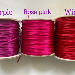 May include: Three spools of cord in different shades of pink: purple, rose pink, and wine. The spools are labeled with the color names.