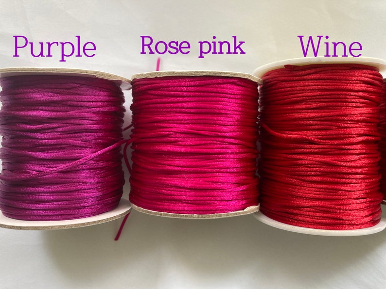 May include: Three spools of cord in different shades of pink: purple, rose pink, and wine. The spools are labeled with the color names.