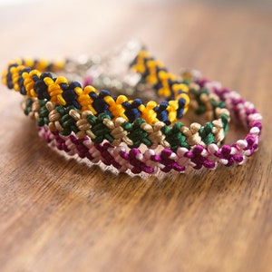 Könnte beinhalten: Vier bunte Freundschaftsarmbänder aus geknüpfter Schnur in Gelb, Dunkelblau, Grün und Rosa.