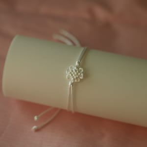 May include: A white string bracelet with a knotted flower design.