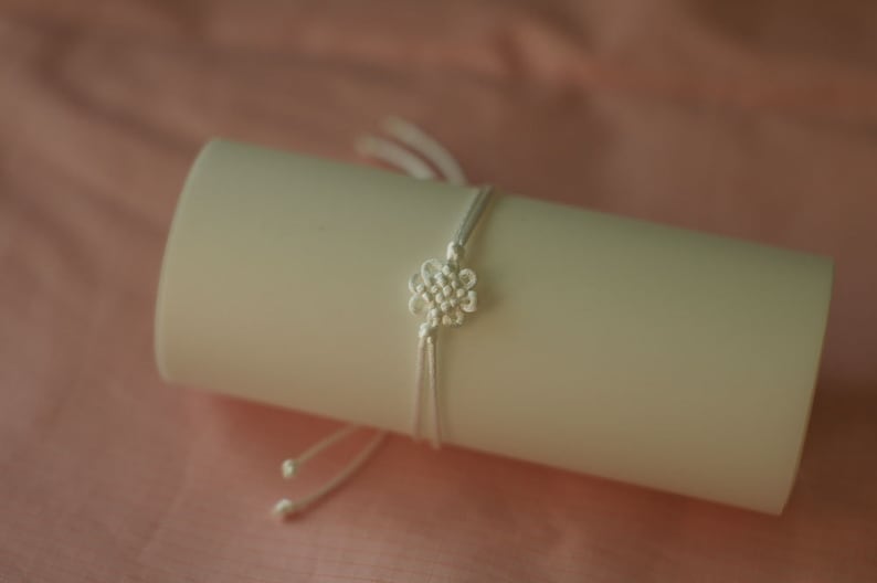 May include: A white string bracelet with a knotted flower design.