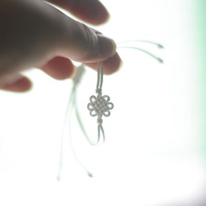 May include: A white string bracelet with a knotted flower design.