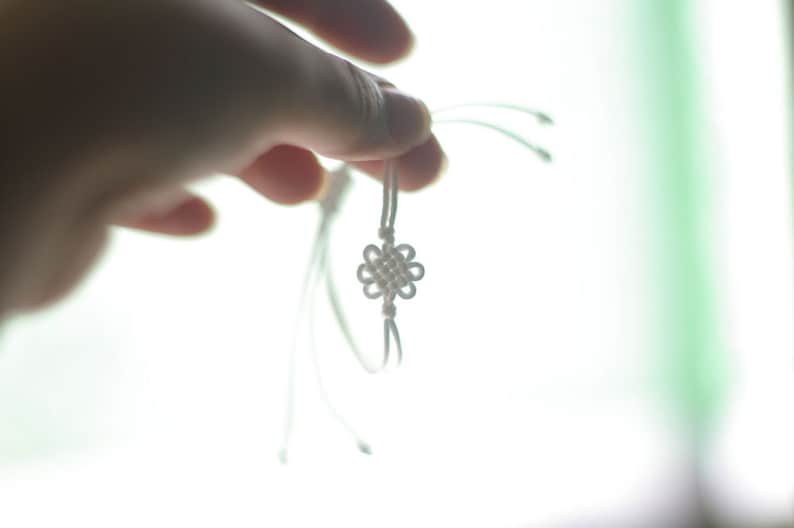May include: A white string bracelet with a knotted flower design.