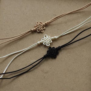 May include: Three knotted cords with decorative knots at the ends. The cords are brown, white, and black.