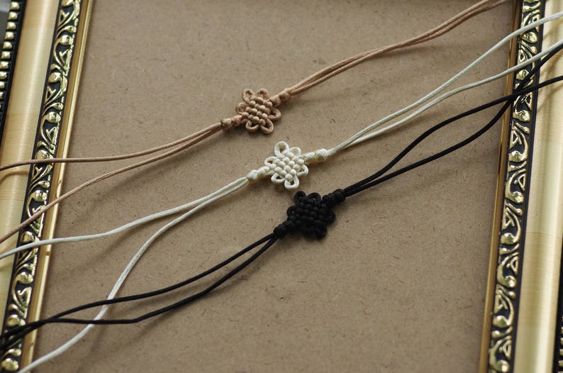 May include: Three knotted cords with decorative knots at the ends. The cords are brown, white, and black.
