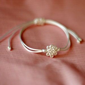May include: A white string bracelet with a white flower-shaped knot in the center.