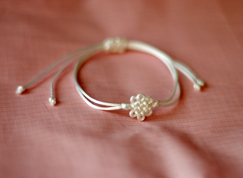 May include: A white string bracelet with a white flower-shaped knot in the center.