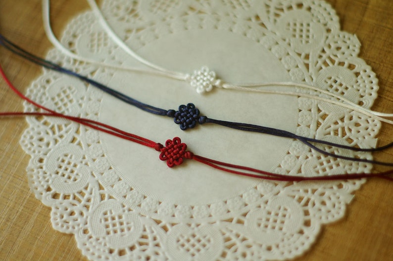 May include: Three knotted cords with decorative flower-shaped ends. The cords are white, navy blue, and red.