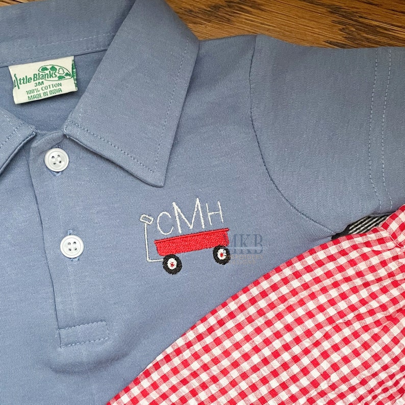Peut inclure: Un polo bleu clair avec un chariot rouge brod&eacute; sur le devant. Le chariot porte les lettres CMH sur le c&ocirc;t&eacute;. Le polo est associ&eacute; &agrave; un short en vichy rouge et blanc.