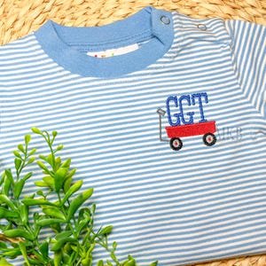 Peut inclure: Un t-shirt b&eacute;b&eacute; ray&eacute; bleu et blanc avec un chariot rouge brod&eacute; sur le devant. Le chariot porte les lettres "GGT".