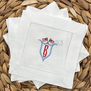 May include: Set of white linen napkins with a blue and red embroidered monogram and two small American flags. The monogram is a capital "B" with a blue shield and red letter.