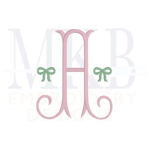May include: Pink monogram with the letter "A" in the center and the letters "M" and "B" on either side. Green bows are on either side of the "A". The text "Embroidery Designs" is below the monogram.