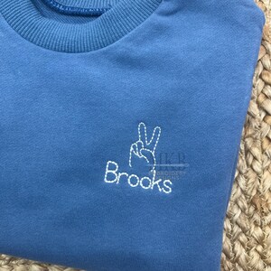 May include: A blue sweatshirt with white embroidery of a peace sign and the word "Brooks".