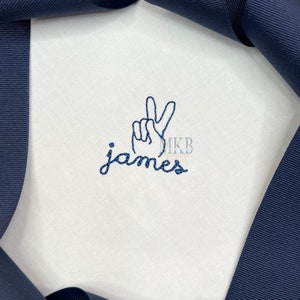 May include: White embroidered baby onesie with a peace sign and the name "James" in blue thread.