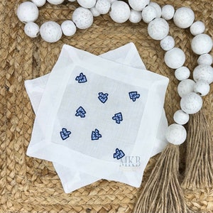 May include: Two white linen cocktail napkins with embroidered blue and navy arrow designs. The napkins are square and have a simple border. The logo "MKB Designs" is visible in the lower right corner.