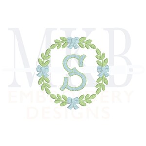 May include: A green wreath with blue bows and a light blue letter "S" in the centre. The wreath is surrounded by the text "MKB EMBROIDERY DESIGNS".