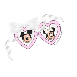 Op de afbeelding: Roze hartvormige zonnebril met Mickey en Minnie Mouse. De zonnebril heeft een witte strik en lint. De tekst "Happily Ever After" staat op de zijkant.