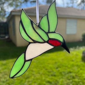 May include: A stained glass hummingbird ornament with green, white, and red accents. The hummingbird is in flight with its wings spread out.