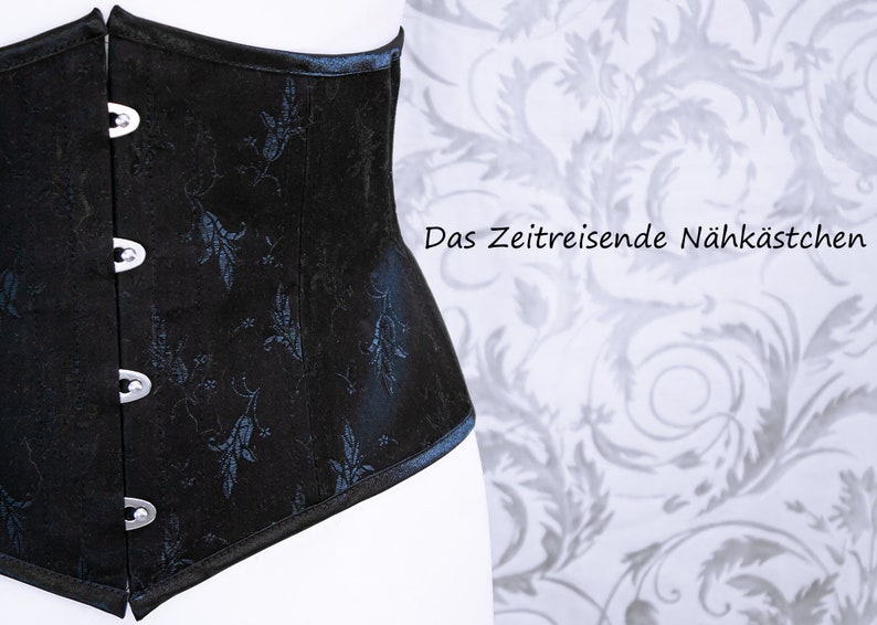 May include: Black corset with silver clasps and a floral pattern. The corset has a structured design and a slight curve. The text "Das Zeitreisende N&auml;hk&auml;stchen" is visible in the background. The corset is a fashion item.