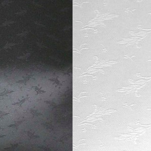 May include: A split image showcasing two fabric samples. One side is black, the other is white. Both have a repeating embossed floral pattern. The texture is visible, with the design slightly raised from the surface.