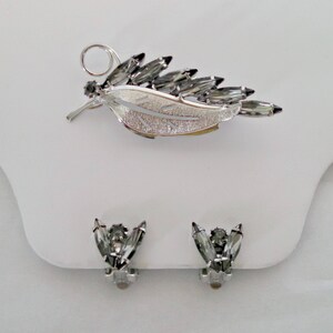 May include: A silver leaf-shaped brooch with clear rhinestones and a matching pair of clip-on earrings with clear rhinestones.